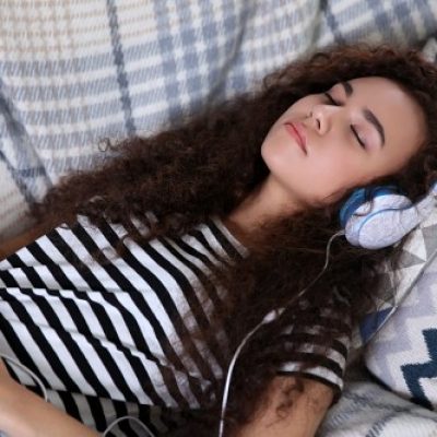 Dm-Harmonics-wie werde ich meine schulden los-Frau liegt mit Kopfhörern im Bett und hört binaurale Beats